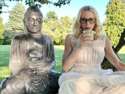 Fazendo carão com um drink na mão ao lado de uma estátua de Buda, Madonna critica Trump